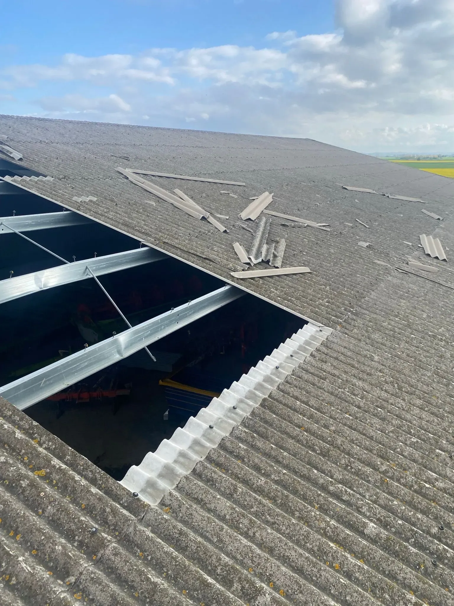 Storm-damaged corrugated roof on an agricultural barn with exposed steel framework and broken panels