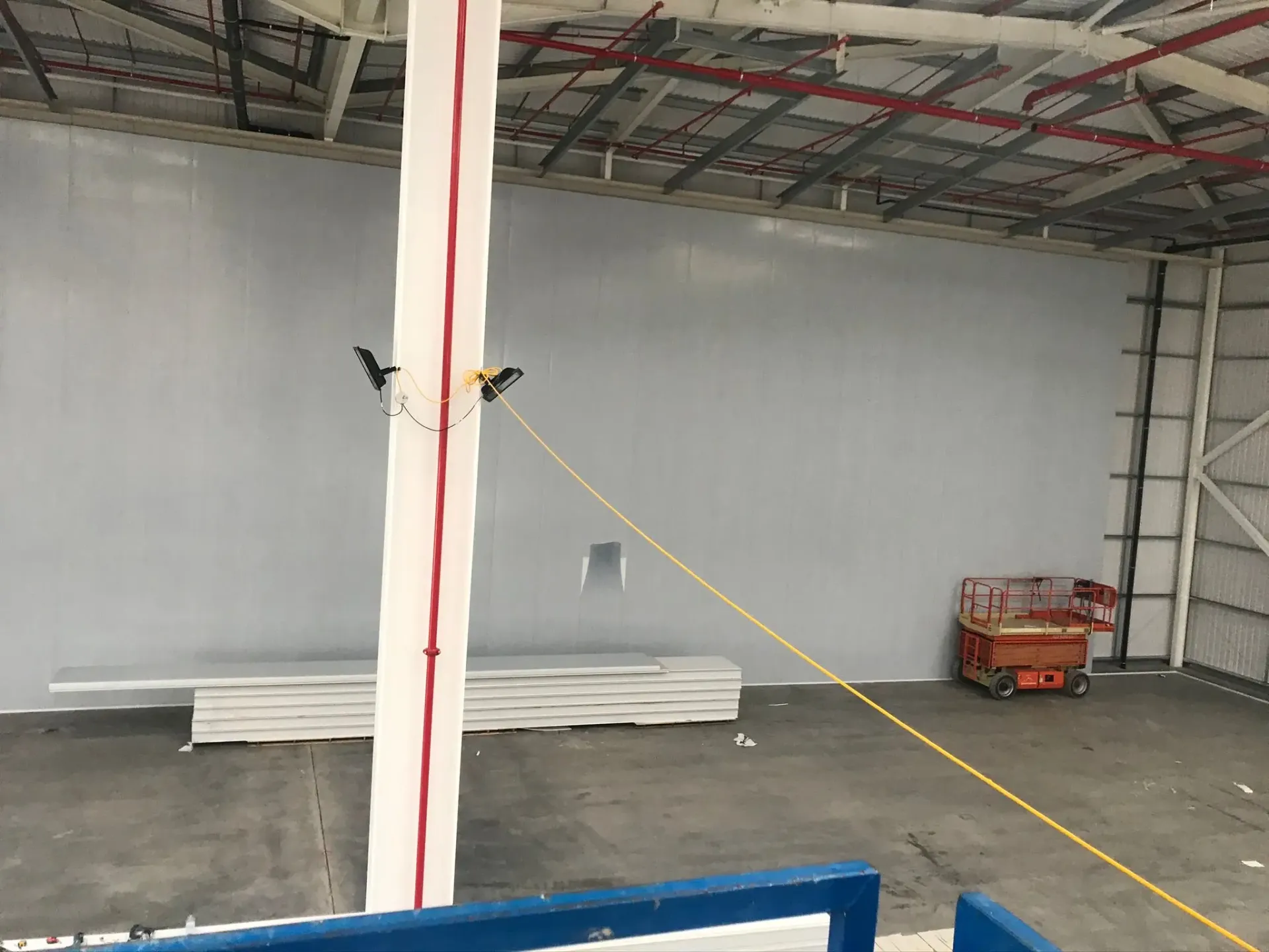 Interior of a newly constructed steel-framed industrial warehouse showing installed wall cladding, a steel support column, and a scissor lift on a concrete floor.