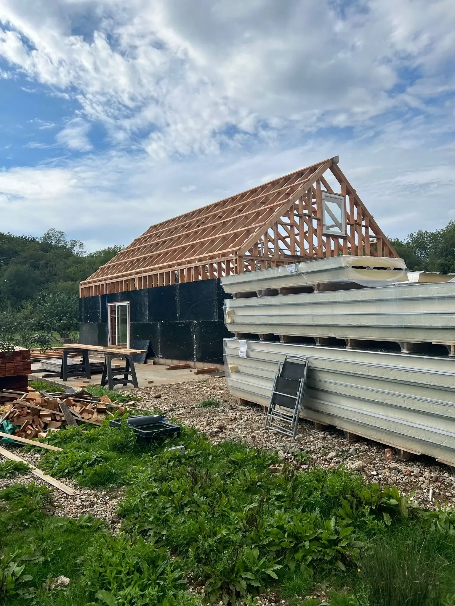 Agricultural shed construction in progress showing an exposed roof frame and stacks of weather-resistant cladding panels waiting to be installed.