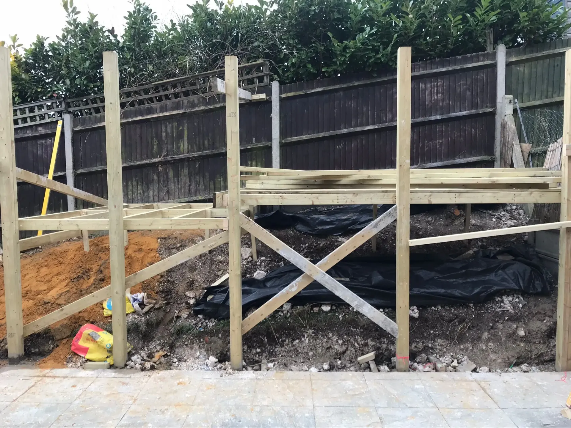 Timber structural subframe being built on a sloped site next to a wooden boundary fence